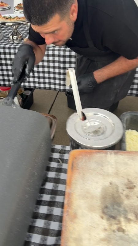 Video still of a chef plating food at an outdoor catering setup with a checkered tablecloth