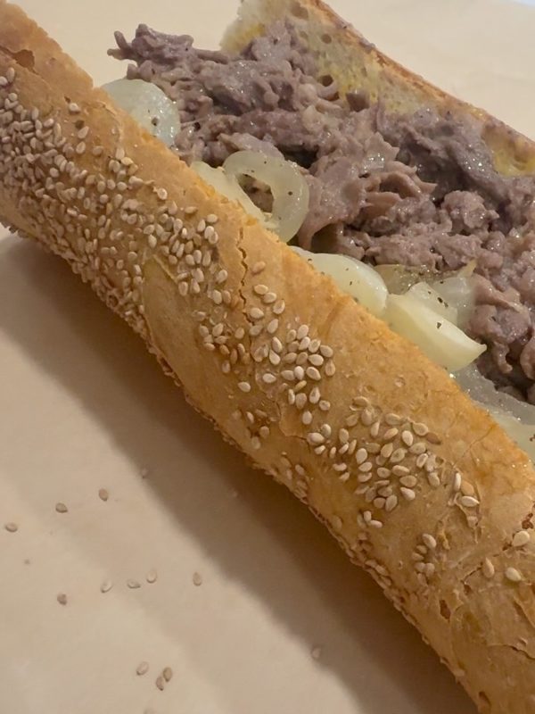 Close-up of a cheesesteak with steak and onions on a sesame-topped roll