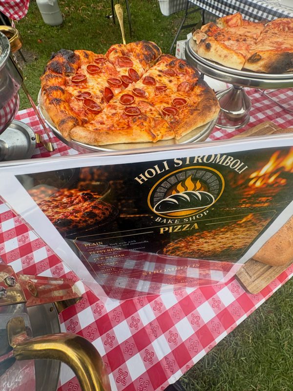 Pepperoni pizza on a stand at an outdoor catering table next to the Holi Stromboli menu sign